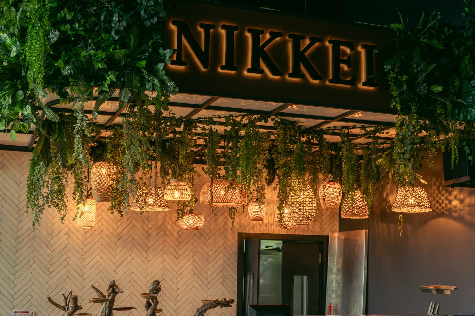 Cartel retroiluminado de la barra Nikkei bajo lámparas de mimbre y vegetación colgante