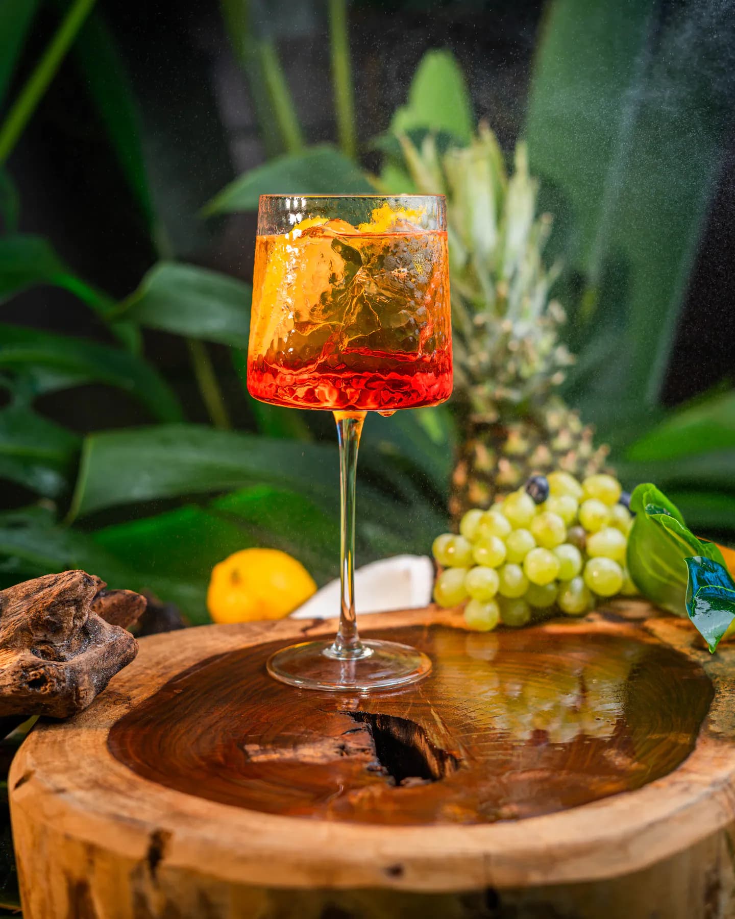 Spritz naranja en copa con hielo sobre un tronco, con ananá y uvas