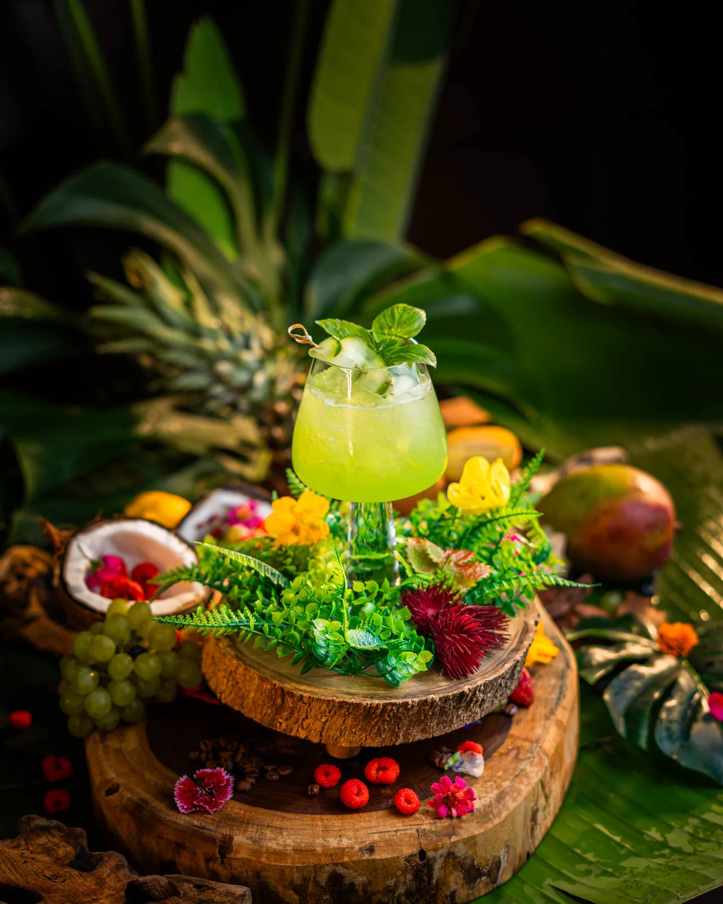 Trago verde con pepino y menta en copa, servido sobre un nido de helechos y flores