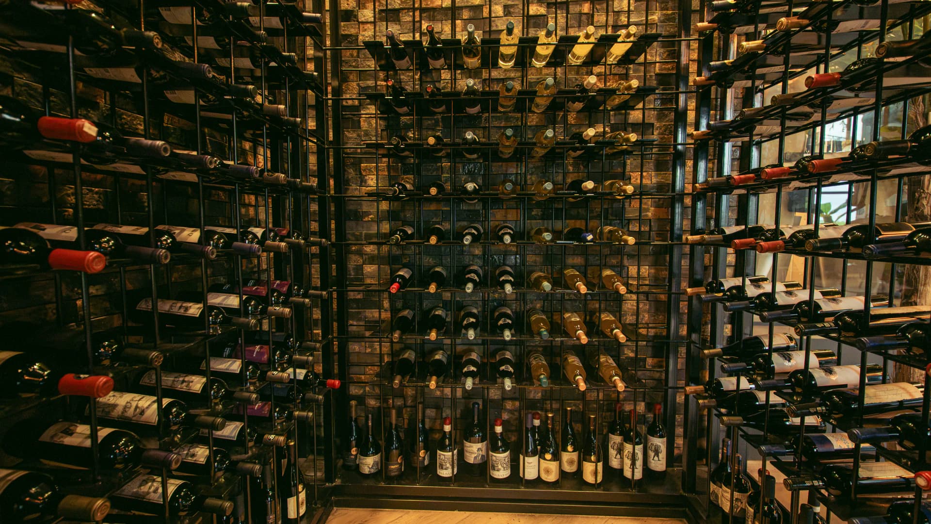Interior de la cava visto de frente, con botellas en estanterías de hierro y pared de piedra